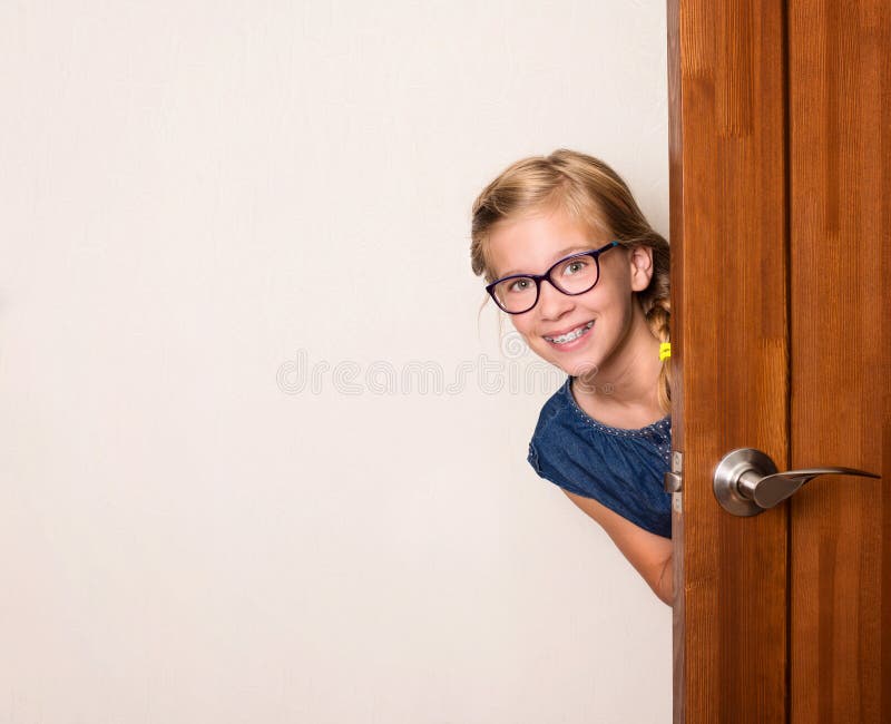 Muchacha linda sonriente feliz en lentes detrás de la puerta en casa fotos de archivo libres de regalías Muchacha linda sonriente feliz en lentes detrás de la puerta en casa fotos de archivo libres de regalías