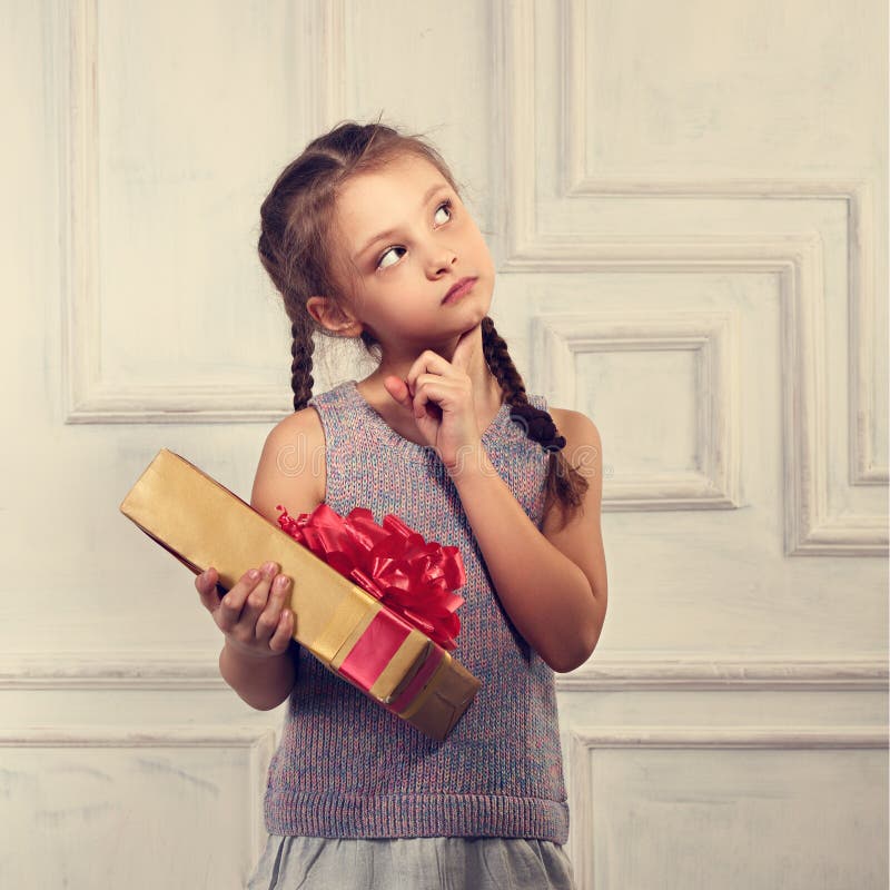 Muchacha linda sonriente hermosa que sostiene la caja del oro con el regalo con el arco rojo y que mira para arriba imagen de archivo libre de regalías Muchacha linda sonriente hermosa que sostiene la caja del oro con el regalo con el arco rojo y que mira para arriba imagen de archivo libre de regalías