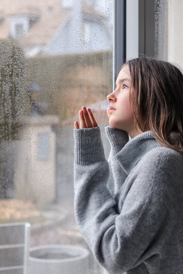 Muchacha melancólica hermosa del adolescente en el suéter gris caliente que mira exterior a través de las gotas de agua en ventan fotografía de archivo Muchacha melancólica hermosa del adolescente en el suéter gris caliente que mira exterior a través de las gotas de agua en ventan fotografía de archivo