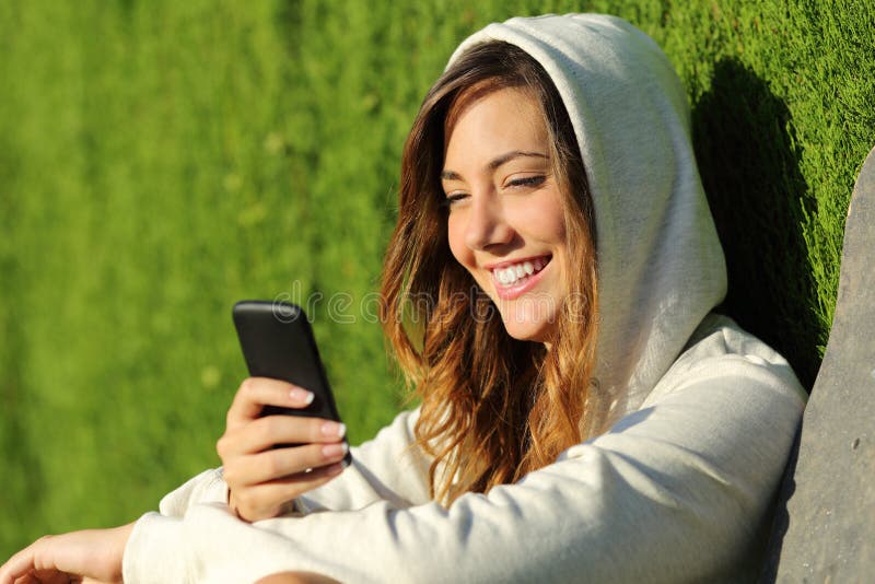 Muchacha moderna del adolescente que usa un teléfono elegante en un parque