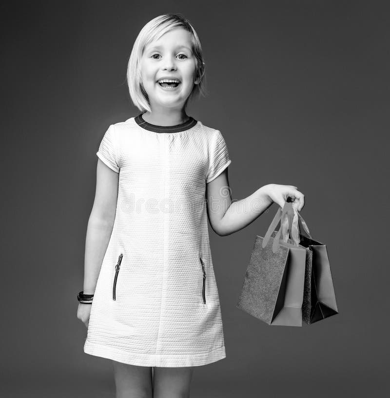 Muchacha moderna feliz en el vestido blanco en el gris que muestra los panieres imágenes de archivo libres de regalías Muchacha moderna feliz en el vestido blanco en el gris que muestra los panieres imágenes de archivo libres de regalías