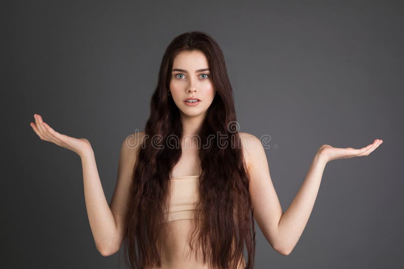 Muchacha morena joven con los hombros desnudos que señala las manos en lado para presentar un producto fotografía de archivo libre de regalías Muchacha morena joven con los hombros desnudos que señala las manos en lado para presentar un producto fotografía de archivo libre de regalías