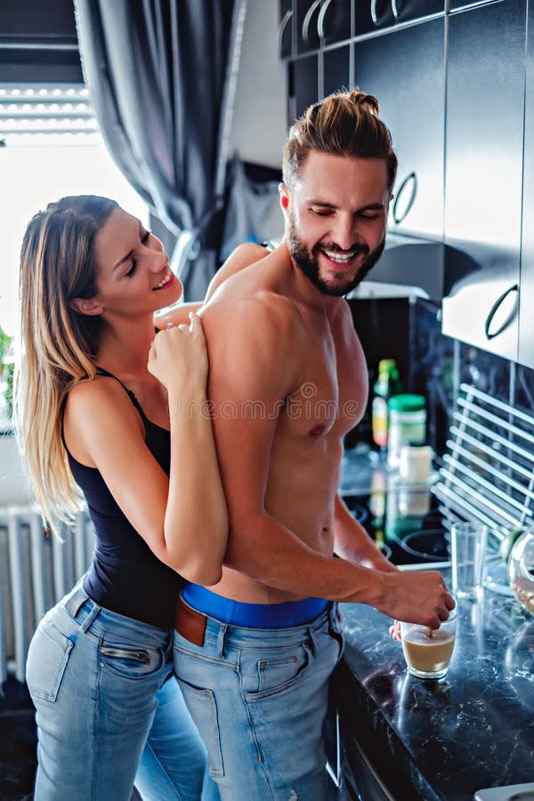 Muchacha que abraza al novio de detrás mientras que él está haciendo el café imagen de archivo libre de regalías Muchacha que abraza al novio de detrás mientras que él está haciendo el café imagen de archivo libre de regalías