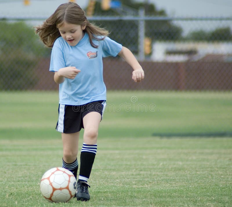 Happy young girl playing football or soccer on grass pitch. Happy young girl playing football or soccer on grass pitch.