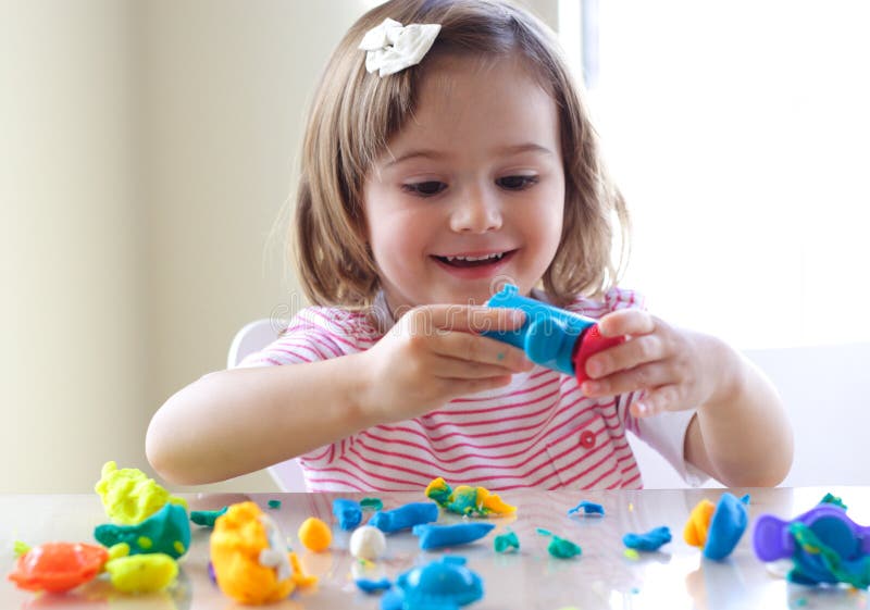 Little girl is learning to use colorful play dough in a well lit room near window. Little girl is learning to use colorful play dough in a well lit room near window