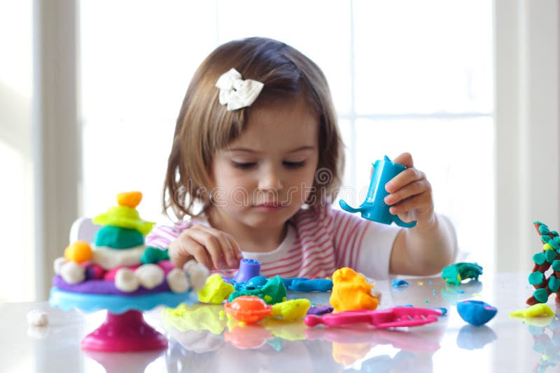 Little girl is learning to use colorful play dough in a well lit room near window. Little girl is learning to use colorful play dough in a well lit room near window