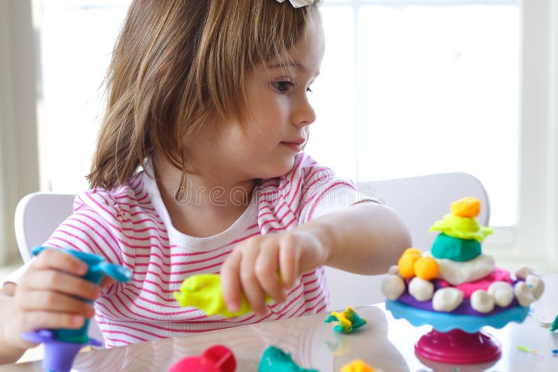 Little girl is learning to use colorful play dough in a well lit room near window. Little girl is learning to use colorful play dough in a well lit room near window