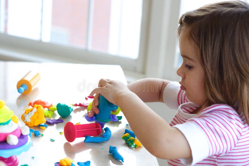 Little girl is learning to use colorful play dough in a well lit room near window. Little girl is learning to use colorful play dough in a well lit room near window