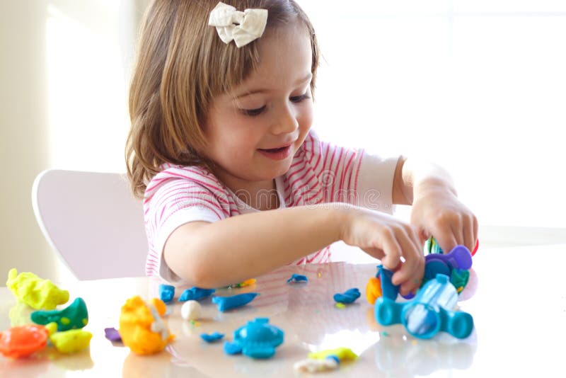 Little girl is learning to use colorful play dough in a well lit room near window. Little girl is learning to use colorful play dough in a well lit room near window