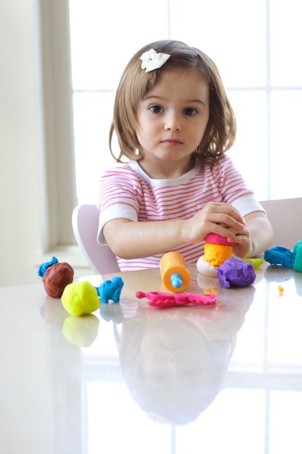 Little girl is learning to use colorful play dough in a well lit room near window. Little girl is learning to use colorful play dough in a well lit room near window