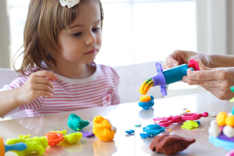 Little girl is learning to use colorful play dough in a well lit room near window. Little girl is learning to use colorful play dough in a well lit room near window