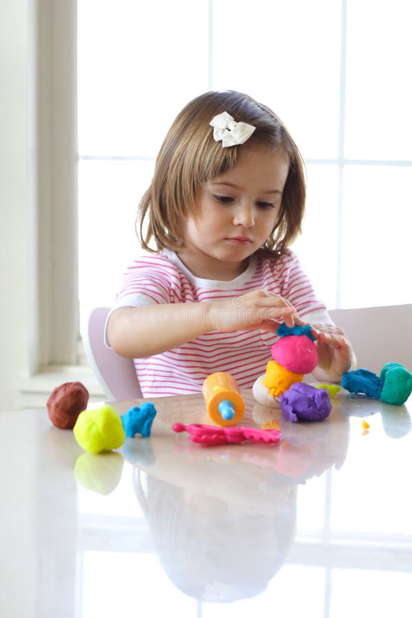 Little girl is learning to use colorful play dough in a well lit room near window. Little girl is learning to use colorful play dough in a well lit room near window