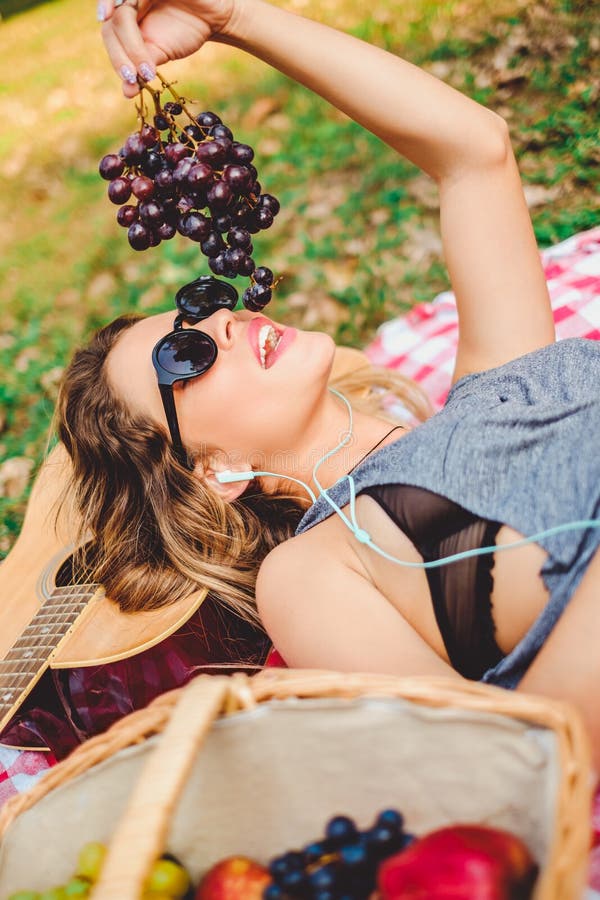 Muchacha que miente en una guitarra y que come las uvas en comida campestre fotos de archivo libres de regalías Muchacha que miente en una guitarra y que come las uvas en comida campestre fotos de archivo libres de regalías