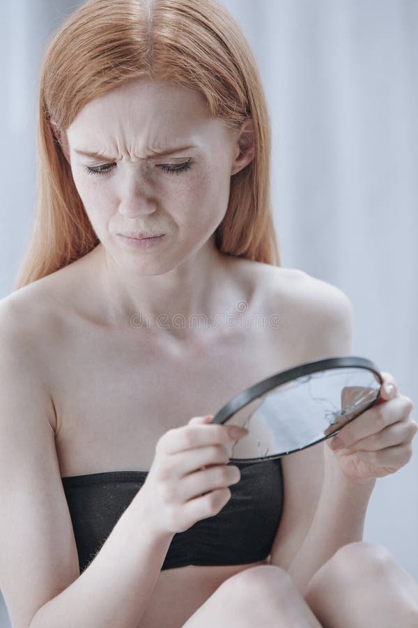 Red hair girl looking into a broken mirror with utter self disgust. Red hair girl looking into a broken mirror with utter self disgust