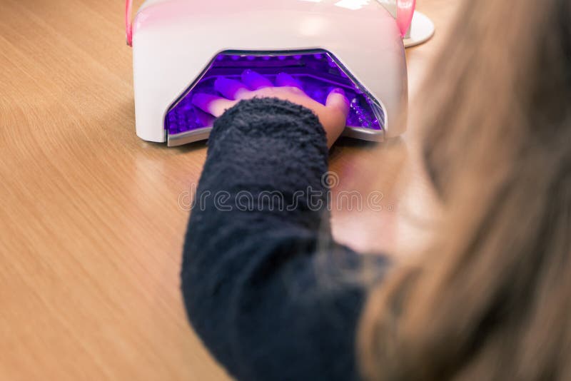 Muchacha que seca al esmalte de uñas debajo de la lámpara imagen de archivo libre de regalías Muchacha que seca al esmalte de uñas debajo de la lámpara imagen de archivo libre de regalías