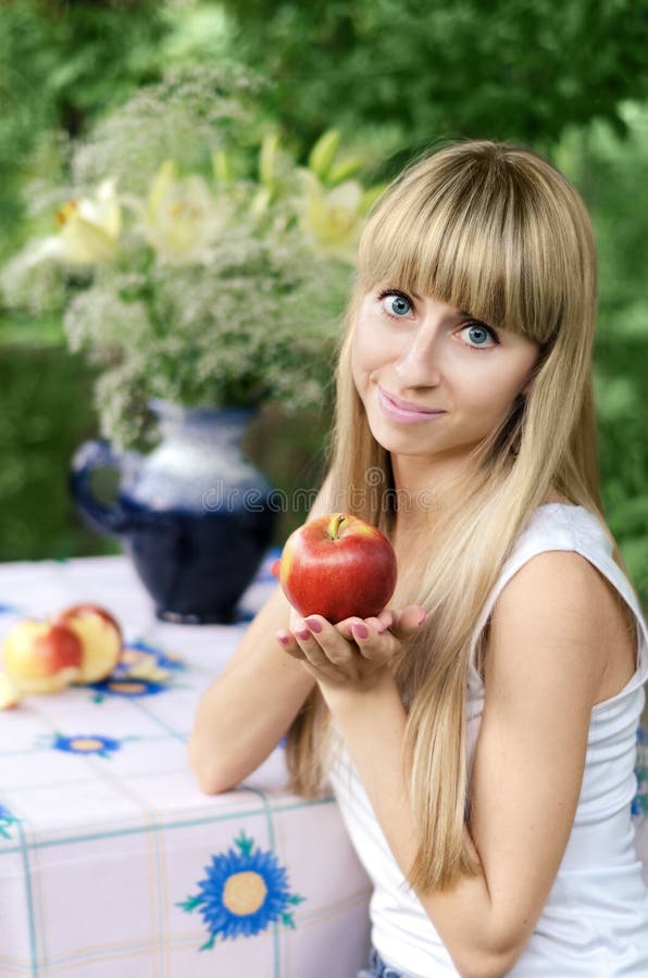 Muchacha que sostiene Apple, sentándose en una tabla en el jardín fotografía de archivo libre de regalías Muchacha que sostiene Apple, sentándose en una tabla en el jardín fotografía de archivo libre de regalías