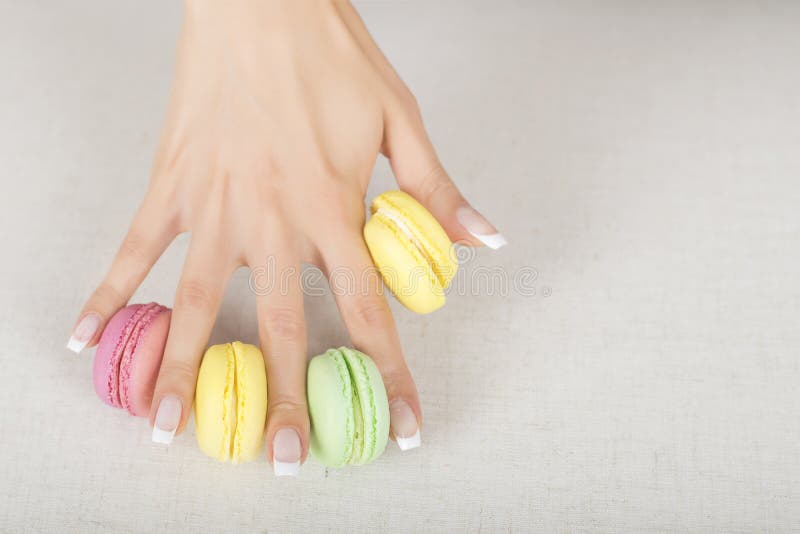 Muchacha que sostiene los macarrones coloridos en manos con la manicura francesa del gel foto de archivo libre de regalías Muchacha que sostiene los macarrones coloridos en manos con la manicura francesa del gel foto de archivo libre de regalías