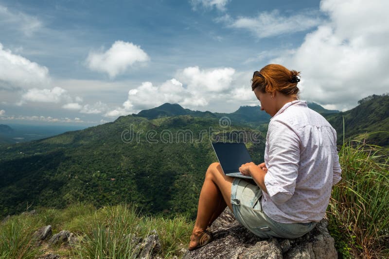 Caucasian girl working on her computer on the top of the mountain. Concept or remote work in internet for frilancer. Caucasian girl working on her computer on the top of the mountain. Concept or remote work in internet for frilancer