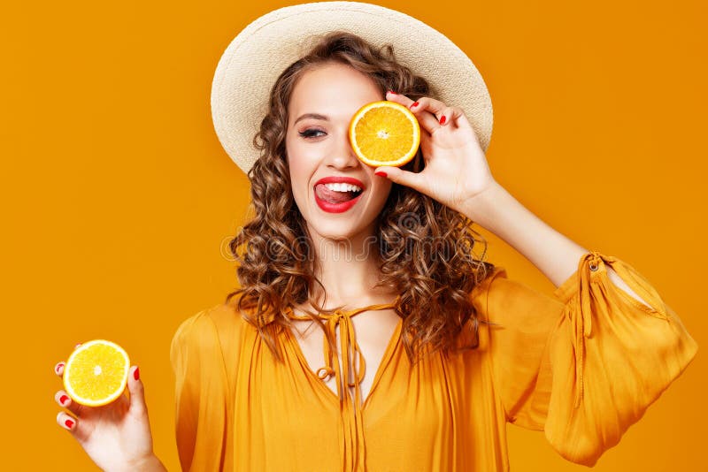 Muchacha rizada joven alegre de la mujer con la naranja en fondo amarillo fotos de archivo libres de regalías