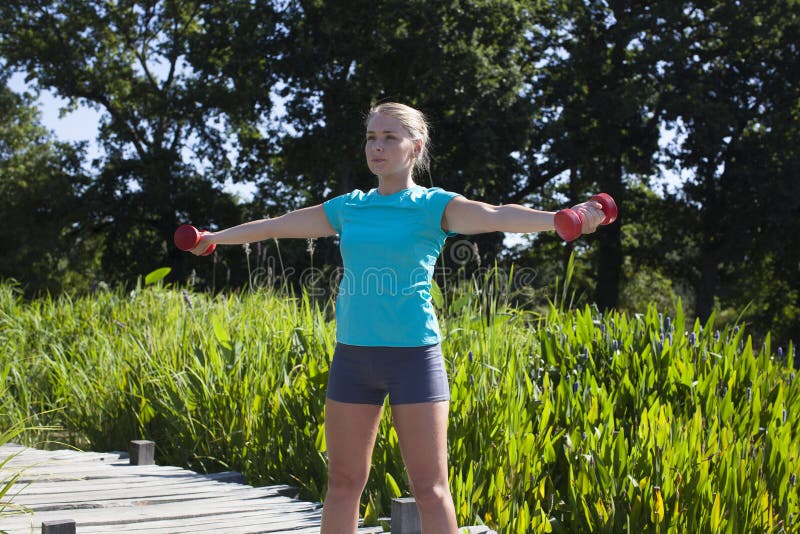 Muchacha rubia atlética que entona para arriba y levantamiento de pesas con pesas de gimnasia, verano imagen de archivo libre de regalías Muchacha rubia atlética que entona para arriba y levantamiento de pesas con pesas de gimnasia, verano imagen de archivo libre de regalías