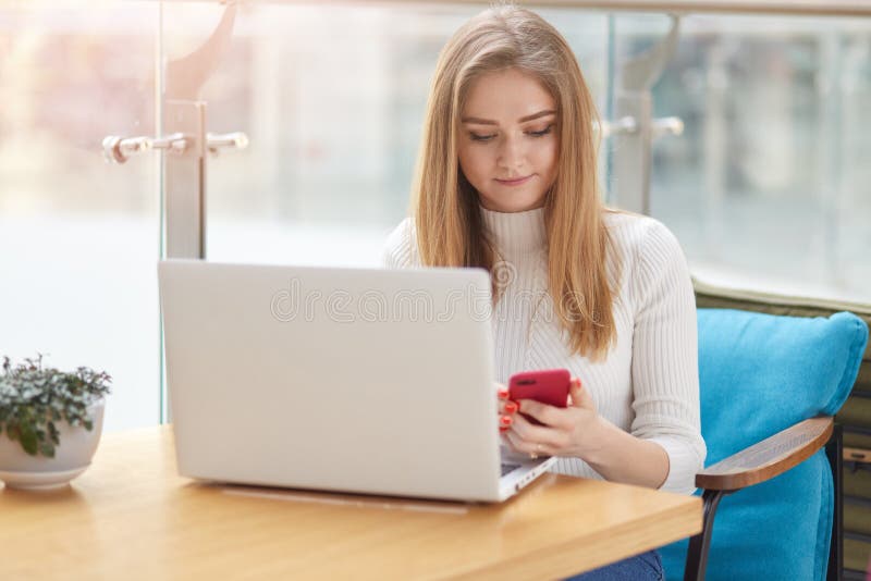 Muchacha rubia de pelo largo concentrada del estudiante que comprueba la red social con el teléfono mientras que teniendo resto e imagenes de archivo Muchacha rubia de pelo largo concentrada del estudiante que comprueba la red social con el teléfono mientras que teniendo resto e imagenes de archivo