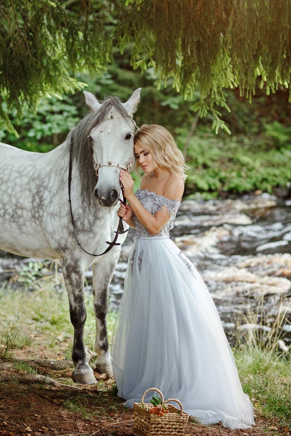 Beautiful slender blond girl in dress hugging a gray horse, outdoors in summer in the forest. Beautiful slender blond girl in dress hugging a gray horse, outdoors in summer in the forest