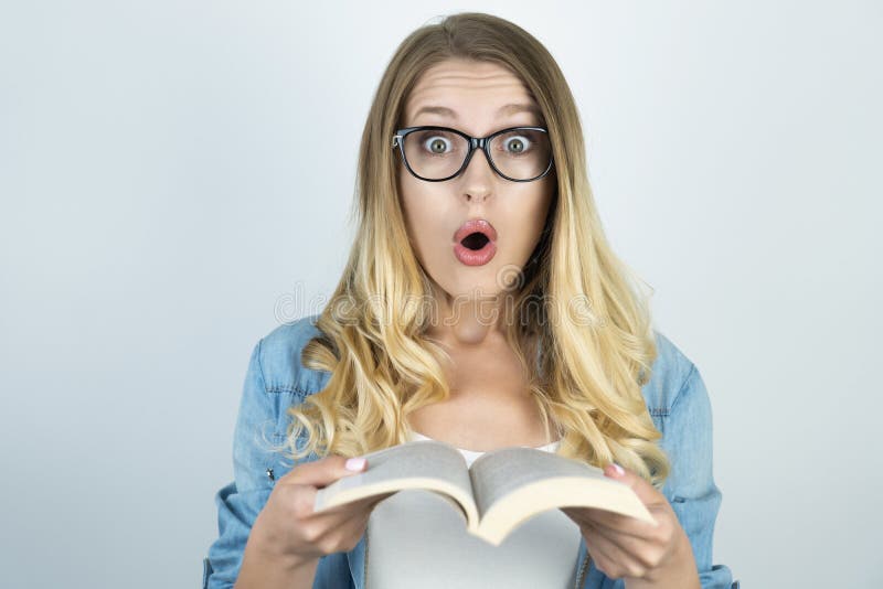 Muchacha rubia en vidrios sorprendida sosteniendo el libro imágenes de archivo libres de regalías Muchacha rubia en vidrios sorprendida sosteniendo el libro imágenes de archivo libres de regalías