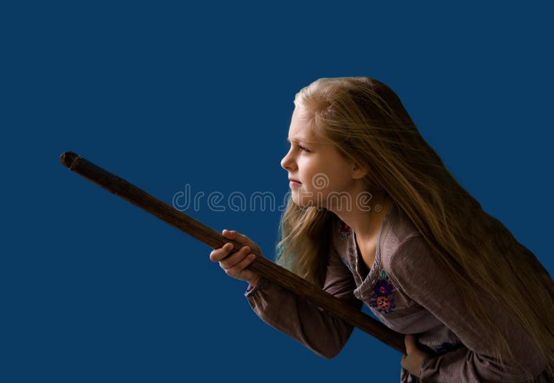 Muchacha rubia hermosa en un palo de escoba bajo la forma de fondo del azul de la bruja fotografía de archivo Muchacha rubia hermosa en un palo de escoba bajo la forma de fondo del azul de la bruja fotografía de archivo