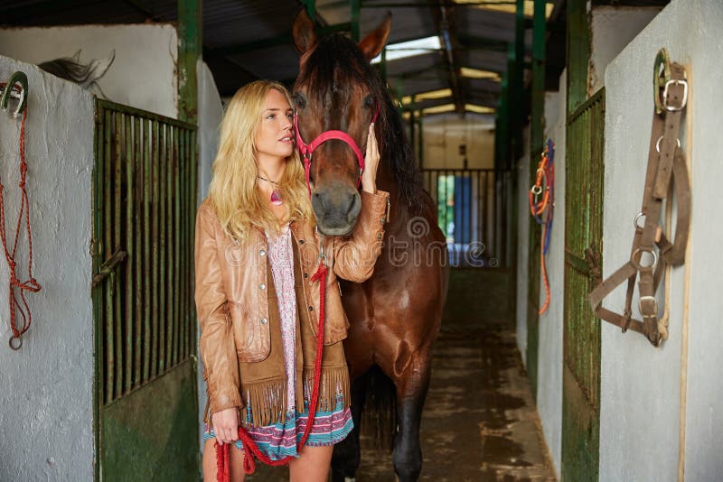 Muchacha rubia que celebra el caballo en el establo foto de archivo libre de regalías Muchacha rubia que celebra el caballo en el establo foto de archivo libre de regalías