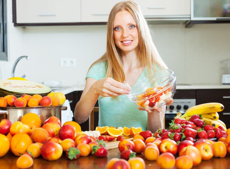 Muchacha rubia que cocina la ensalada de fruta con las frutas imágenes de archivo libres de regalías Muchacha rubia que cocina la ensalada de fruta con las frutas imágenes de archivo libres de regalías