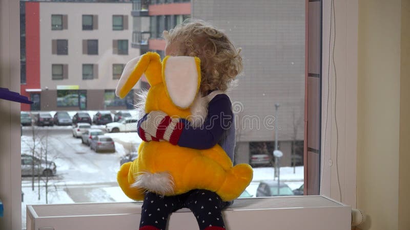 Muchacha sentada con un gran conejo al borde de la ventana. está nevando fuera de la ventana 4k