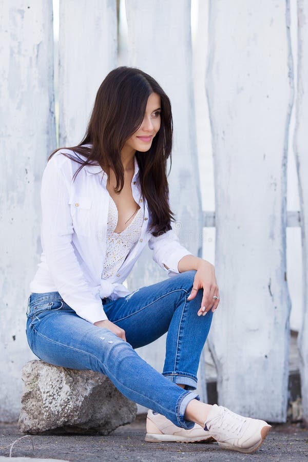 Muchacha sonriente hermosa que lleva la camisa blanca en blanco y vaqueros que presentan contra la pared de madera de la calle Ro imagen de archivo Muchacha sonriente hermosa que lleva la camisa blanca en blanco y vaqueros que presentan contra la pared de madera de la calle Ro imagen de archivo