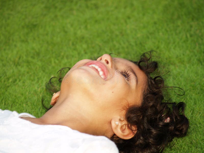 Closeup of a happy, smiling, young asian girl with dark curly hair, laying in the grass and looking up. Closeup of a happy, smiling, young asian girl with dark curly hair, laying in the grass and looking up.