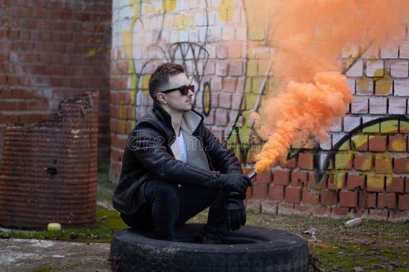 Muchacho con ropa y gafas de sol modernas con una llamarada del humo en un lugar abandonado imagenes de archivo Muchacho con ropa y gafas de sol modernas con una llamarada del humo en un lugar abandonado imagenes de archivo