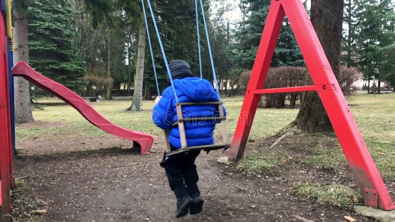 Muchacho de la edad del preescolar en el oscilación en el parque de detrás - la cámara lenta Muchacho joven que juega solamente e almacen de video