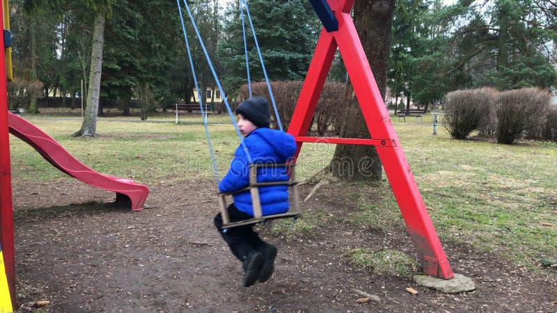 Muchacho de la edad del preescolar en el oscilación en el parque de detrás Muchacho joven que juega solamente en el oscilación en metrajes