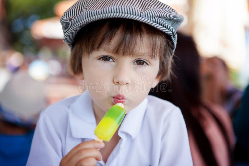 Muchacho dulce lindo, niño, comiendo el helado colorido en el parque fotografía de archivo Muchacho dulce lindo, niño, comiendo el helado colorido en el parque fotografía de archivo