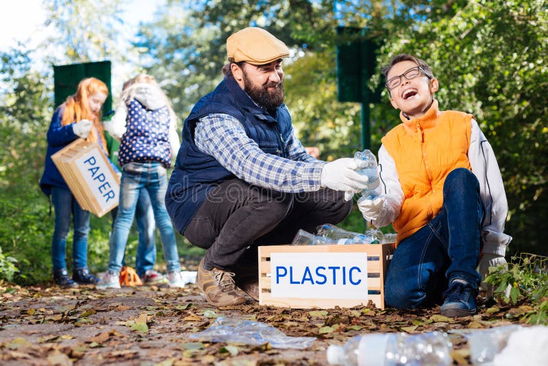 Muchacho joven agradable positivo que recoge las botellas plásticas imagen de archivo