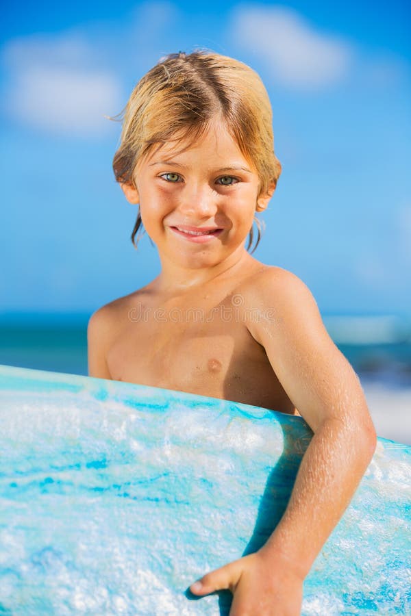 Muchacho joven feliz en la playa con la tabla hawaiana