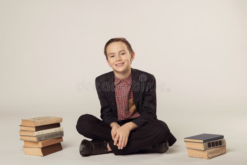 Muchacho lindo en un traje que se sienta en un fondo blanco Pila de libros fotos de archivo Muchacho lindo en un traje que se sienta en un fondo blanco Pila de libros fotos de archivo