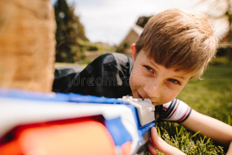 Muchacho lindo que juega con el arma del juguete en patio imagen de archivo Muchacho lindo que juega con el arma del juguete en patio imagen de archivo