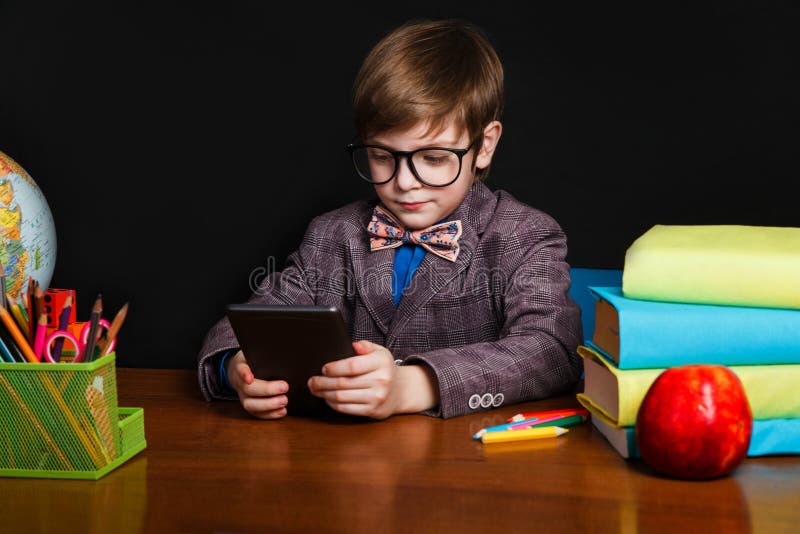 Muchacho lindo que lee un eBook y que se sienta en un escritorio de la escuela De nuevo a escuela fotos de archivo Muchacho lindo que lee un eBook y que se sienta en un escritorio de la escuela De nuevo a escuela fotos de archivo