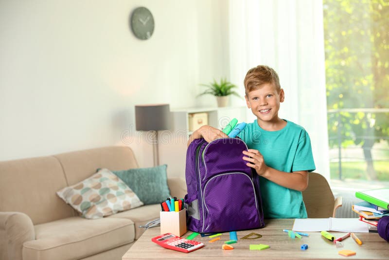 Muchacho lindo que pone los efectos de escritorio de la escuela en la mochila imagenes de archivo Muchacho lindo que pone los efectos de escritorio de la escuela en la mochila imagenes de archivo