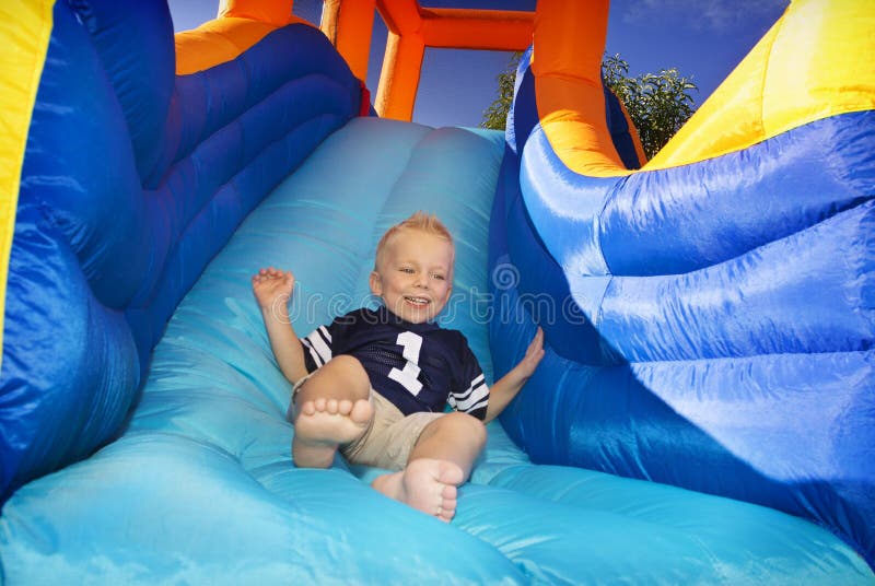 Muchacho que desliza abajo una diapositiva inflable imágenes de archivo libres de regalías Muchacho que desliza abajo una diapositiva inflable imágenes de archivo libres de regalías