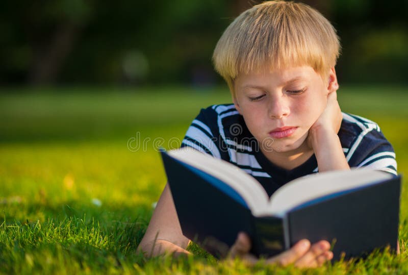 The boy reads the book, lying on the grass. The boy reads the book, lying on the grass.