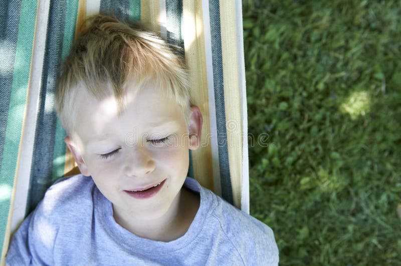 Muchacho rubio del pequeño niño lindo que balancea y que se relaja en una hamaca imagen de archivo libre de regalías Muchacho rubio del pequeño niño lindo que balancea y que se relaja en una hamaca imagen de archivo libre de regalías