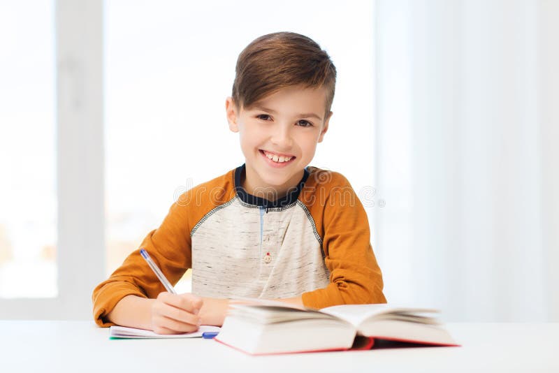 Muchacho sonriente del estudiante que escribe al cuaderno en casa foto de archivo libre de regalías Muchacho sonriente del estudiante que escribe al cuaderno en casa foto de archivo libre de regalías