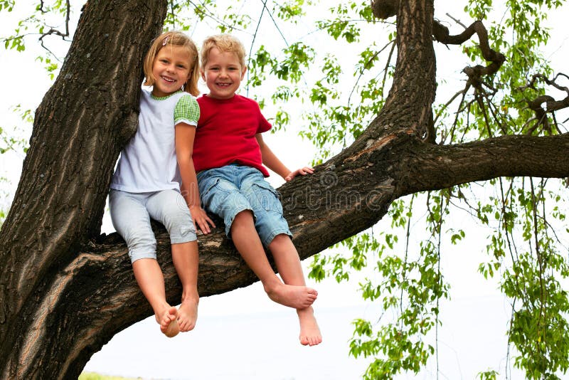 Muchacho y muchacha que se sientan en un árbol foto de archivo Muchacho y muchacha que se sientan en un árbol foto de archivo