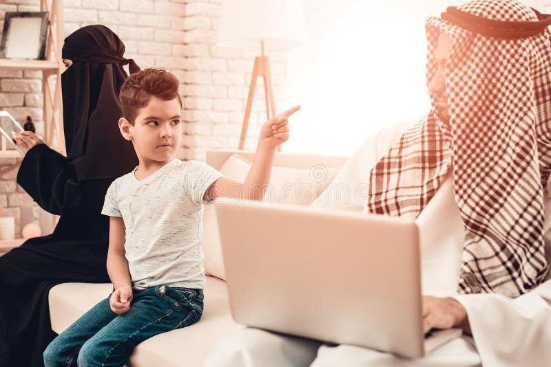 Muchacho árabe aburrido que se sienta con la familia en el sofá foto de archivo libre de regalías Muchacho árabe aburrido que se sienta con la familia en el sofá foto de archivo libre de regalías
