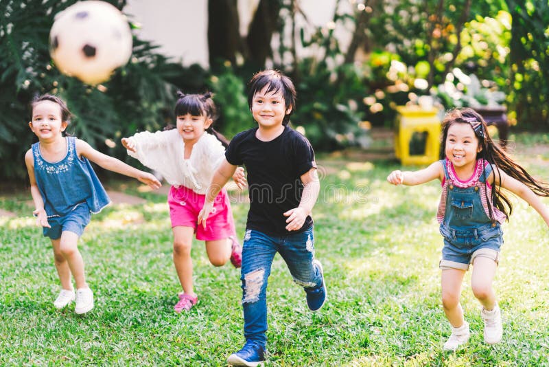 Muchachos felices del asiático y de la raza mixta que corren jugando al fútbol junto en jardín grupo Multi-étnico de los niños, e
